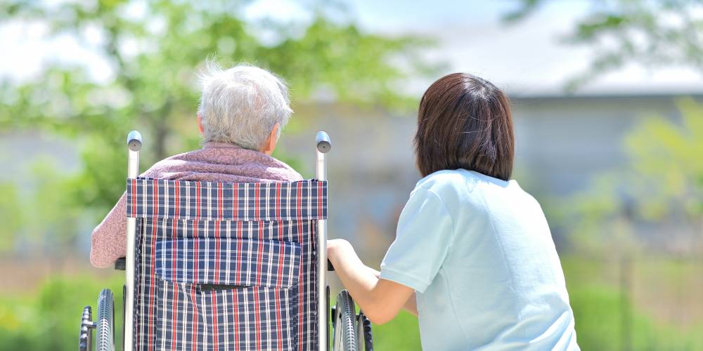 後ろ向きの車いすおばあさんと介護士の女性